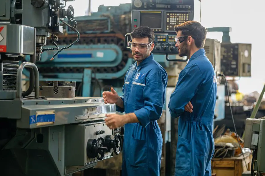 Two technicians in coveralls talking through equipment on a machine floor